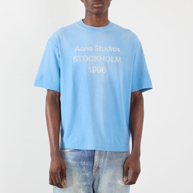 Model wearing Acne Sprayed Logo T-Shirt in cornflower blue with distressed stamp logo print, styled with bleached jeans.