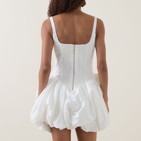 Model wearing Aje Alani Puff-Skirt Mini Dress in ivory, showing rear view with corset bodice, gold back zip, and voluminous bubble skirt.