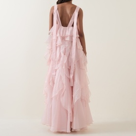 Model wearing Aje Athena Ruffle Gown in Tea Blossom, showing low U-shaped back, tiered ruffles, and maxi length silhouette.