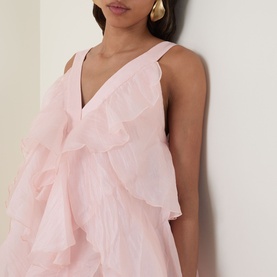 Model wearing Aje Athena Ruffle Gown in Tea Blossom, featuring V-neckline and tiered ruffles. Styled with gold drop earrings.