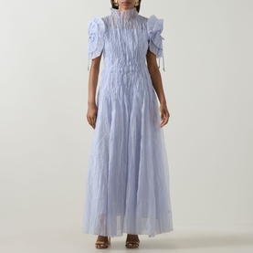 Model wearing Aje Clara Pintuck Dress in French Blue; maxi length tulle with pintuck detail, puff sleeves, tassel trim and high neckline.