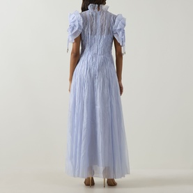 Model wearing Aje Clara Pintuck Dress in French Blue; rear view showing pintuck detail, tassel-trimmed puff sleeves and maxi length.
