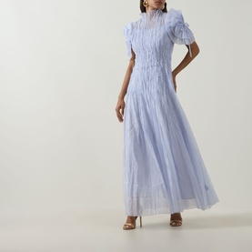 Model wearing Aje Clara Pintuck Dress in French Blue, maxi length with pintuck detail, puff sleeves and high neckline, styled with tan heeled sandals