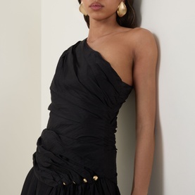 Model wearing black one-shoulder ruched top with gold button detail, styled with matching black skirt and gold drop earrings