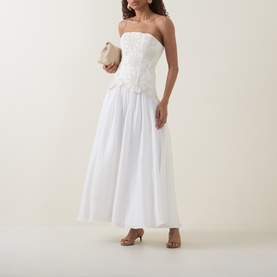 Model wearing Aje Gia Embroidered Off-The-Shoulder Gown in ivory, styled with a cream clutch bag and tan heeled sandals.