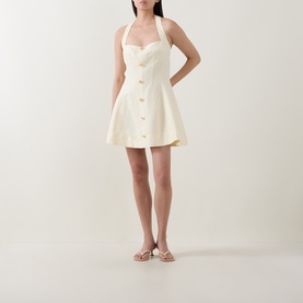 Model wearing Aje Monroe Halter Mini Dress in Butter, featuring halter neck, front metal buttons and A-line silhouette, styled with strappy flat