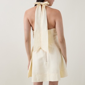 Model wearing Aje Monroe Halter Mini Dress in Butter, showing open back with tie halter neck and A-line silhouette
