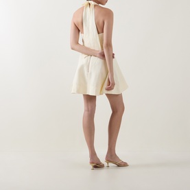 Model wearing Aje Monroe Halter Mini Dress in Butter, halter neck, A-line silhouette, styled with nude kitten heel mules.