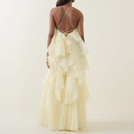 Model wearing Aje Pandorea Ruffle Dress in butter, showing criss-cross back straps, back tie fastening, and tiered ruffle maxi skirt
