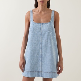 Model wearing Aje Lucina Studded Denim Mini Dress in light wash blue with square neck, sleeveless silhouette and allover stud detail.