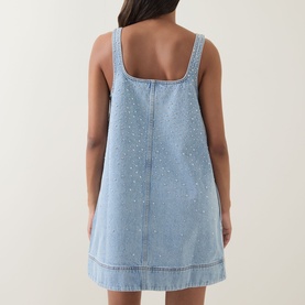 Model wearing Aje Lucina Studded Denim Mini Dress in light wash blue, rear view showing stud detail, square neck and twin needle stitching.