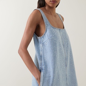 Model wearing Aje Lucina Studded Denim Mini Dress in light wash blue with square neck, sleeveless silhouette and allover stud detail.