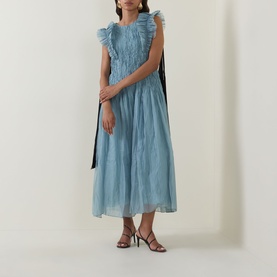 Model wearing Aje Mathilde Dress in Duck Egg; ruffle shoulders, pintuck midi silhouette, contrast tie detail, styled with strappy heels.