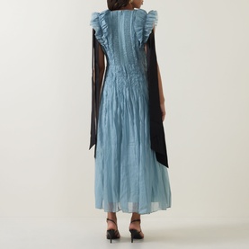 Model wearing Aje Mathilde Dress in Duck Egg with ruffle shoulders, contrast black tie sleeves, pintuck detail, and midi length. Back view.