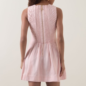 Model wearing Aje Medea Pleated Mini Dress in Tea Blossom, showing back zip, sleeveless design, pleated bodice and ruffled skirt.