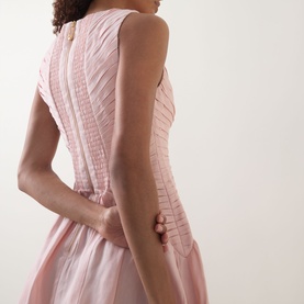 Model wearing Aje Medea Pleated Mini Dress in Tea Blossom, showing back detail with pleated bodice, back zipper, and sleeveless silhouette