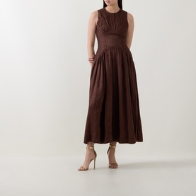 Model wearing Aje Dark Chocolate linen-viscose midi dress with ruched bodice, full skirt, and sleeveless silhouette, styled with strappy heels.