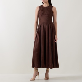 Model wearing Aje Dark Chocolate linen-viscose midi dress with ruched bodice, sleeveless, flared skirt, styled with nude heeled sandals.