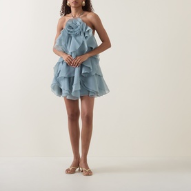 Model wearing Aje Pandorea Ruffled Mini Dress in Duck Egg, strapless with tiered ruffles and 3D floral detail, styled with gold flat sandals