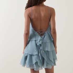 Model wearing Aje Pandorea Ruffled Mini Dress in Duck Egg, showing lace-up open back detail and tiered ruffle skirt