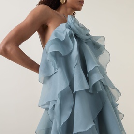 Model wearing Aje Pandorea Ruffled Mini Dress in Duck Egg, featuring tiered ruffle detailing and one-shoulder silhouette, styled with gold earrings