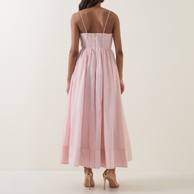 Model wearing Aje Rosie Dress in Tea Blossom, rear view showing back zip, gathered midi skirt and shoulder straps, styled with nude heels.