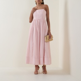 Model wearing Aje Rosie Dress in Tea Blossom; straight neckline, shoulder straps, gathered midi skirt. Styled with nude heels and a small clutch.
