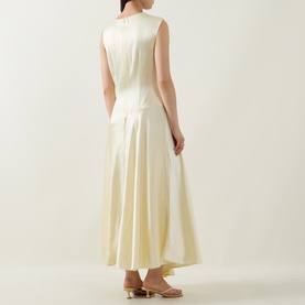 Model wearing Aje Siren Ruffled Dress in Butter, sleeveless midi with asymmetric hemline and back zipper, rear view, styled with tan heels.