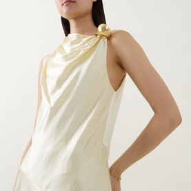Model wearing Aje Siren Ruffled Dress in Butter, sleeveless halterneck with gold-toned hardware detail at shoulder, smooth finish fabric