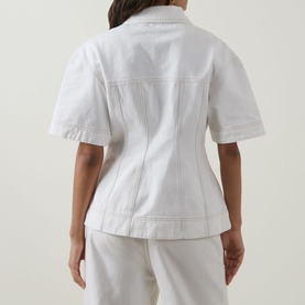 Model wearing Aje Liliana Denim Shirt in ivory, rear view showing shaping seams, fitted waist, and short sleeves, styled with white trousers