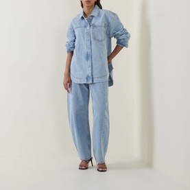Model wearing Aje Lucina High-Rise Stud Barrel Jeans in Light Wash Blue with matching denim shirt and brown heeled sandals.