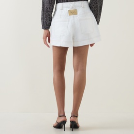 Model wearing Aje ivory cotton shorts with logo patch waistband, styled with black heels and dark floral top, seen from behind
