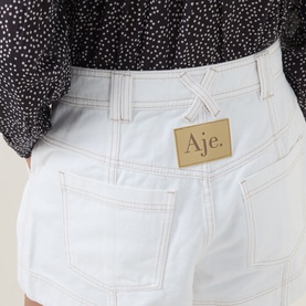 Model wearing Aje ivory cotton shorts with contrast stitching and patch pockets, styled with a black spotted top.