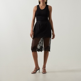 Model wearing Aje Ophelia Lace-Trim Skirt in black with sheer lace hem, styled with black tank top and strappy heels