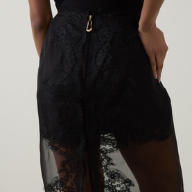Model wearing Aje Ophelia Lace-Trim Skirt in black, showing lace hem detail, sheer overlay, and gold hook-and-eye zip closure at waist.