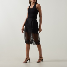 Model wearing Aje Ophelia Lace-Trim Skirt in black with sheer lace hem, styled with a black tank top and strappy heels.