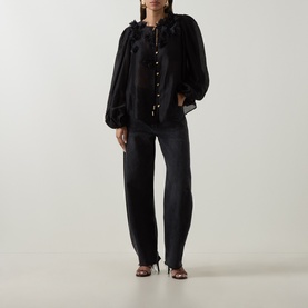 Model wearing Aje Demi Blouse in black with floral appliqu&eacute; neckline and blouson sleeves, styled with dark wide-leg jeans and heeled sandals.