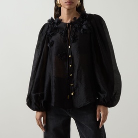 Model wearing Aje Demi Blouse in black with floral appliqu&eacute; neckline, blouson sleeves and gold button front. Styled with dark jeans.