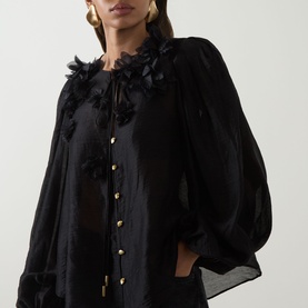 Model wearing Aje Demi Blouse in black with floral appliqu&eacute; neckline, gold button front, and blouson sleeves with subtle sheen.