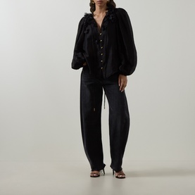 Model wearing Aje Demi Blouse in black with floral appliqu&eacute; neckline and blouson sleeves, styled with wide-leg trousers and heeled sandals.