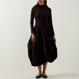Model wearing HIGH brown dress with high neck, long sleeves, and voluminous balloon skirt; styled with black flat shoes