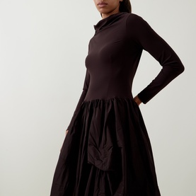 Model wearing HIGH brown long-sleeve dress with fitted turtleneck bodice and voluminous gathered skirt, hand on hip