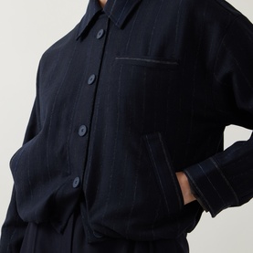 Model wearing HIGH navy pinstripe jacket with button front, chest pocket, and cuffed sleeves, hand in pocket