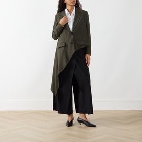 Model wearing HIGH khaki wool-lyocell draped asymmetric jacket with black wide-leg trousers and black kitten heel mules.
