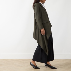 Model wearing HIGH khaki wool-lyocell jacket with draped asymmetric hem, styled with black wide-leg trousers and heeled mules.