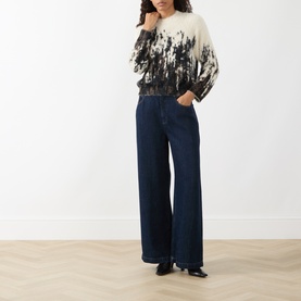 Model wearing HIGH multi-coloured floral print knitwear with wide-leg dark indigo jeans and black pointed-toe flats.