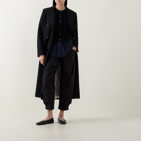 Model wearing HIGH black shirt in layered outfit with long black coat, tapered trousers and black ballet flats.