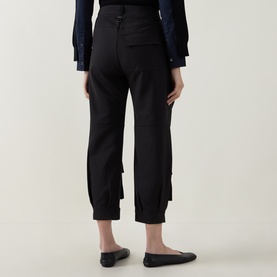 Model wearing HIGH black trousers with gathered cuffed ankles, styled with a navy blue top and black flat shoes, rear view.