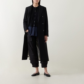 Model wearing HIGH black cargo-style trousers with a long black double-breasted coat, navy top and black flat shoes.