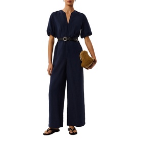 Model wearing Whistles blue wide-leg jumpsuit with V-neck and puff sleeves, styled with brown belt, tan bag and black sandals